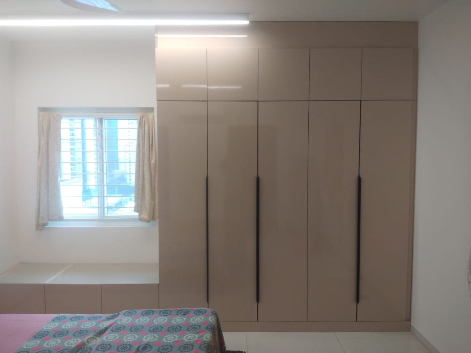 Bedroom wardrobe in warm beige high-gloss finish with slim dark vertical pulls.
